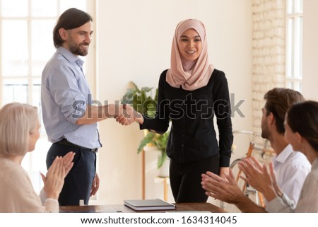Smiling multicultural business partners shake hands close deal make agreement at company briefing in office, happy multiethnic diverse colleagues businesspeople handshake greeting with work promotion