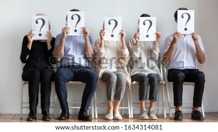 Diverse employees sit on chairs in row hold sheets papers with question marks hide faces, unknown male and women job candidates waiting for interview or recruitment talk in office, employment concept Royalty-Free Stock Photo #1634314081