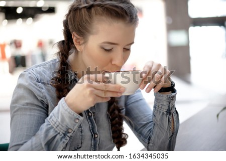 Beautiful woman in jeans shirt  holding cup of coffee and drink in cafe with  in shopping center.