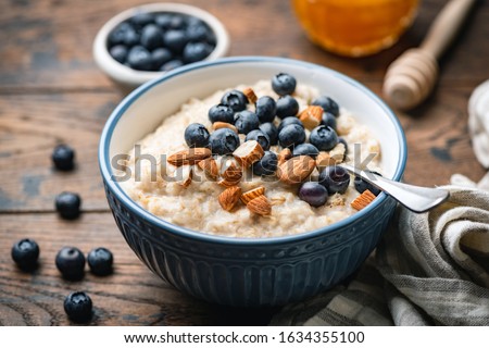 Oatmeal porridge with blueberries, almonds in bowl on wooden table background. Healthy breakfast food Royalty-Free Stock Photo #1634355100