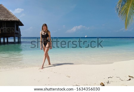 girl in a black swimsuit is walking along the beach