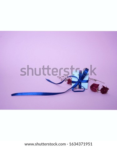 blue gift box with blue ribbon and dried flowers of roses on a gently pink background