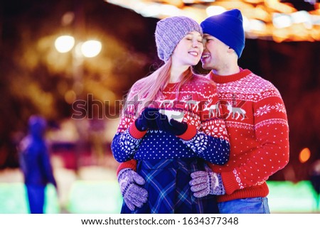 Loving couple drinks hot tea or coffee from thermos mugs on winter street in ice rink night illumination.