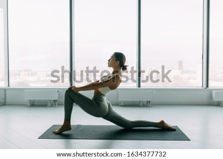 Stretching in the white room by the window. Beautiful girl athlete on the Mat. Flexibility exercises on a light background. 
