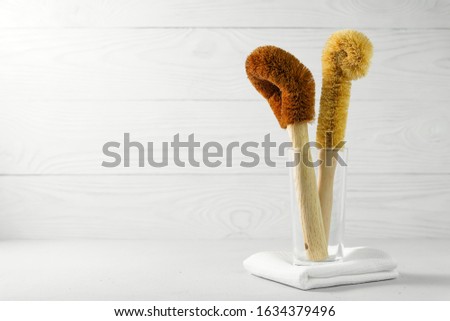 Two coconut scrapers with a bamboo handle in a glass cup on a light background. Biodegradable kitchen accessories for washing dishes and zero waste concept. Image contains copy space.