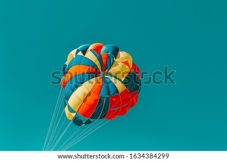 Parachute parasailing of tourists on a sandy beach Sunny weather against the background of clear sea and ocean.The wind blows up the canopy of the parachute against a clear blue sky with clouds Royalty-Free Stock Photo #1634384299