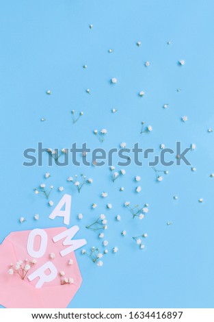 Small white flowers, pink envelope and word AMOR on a light blue background top view