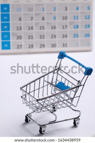 Miniature shopping cart with desktop calendar on white background. Holiday shopping, black friday, monthly special offer concept 