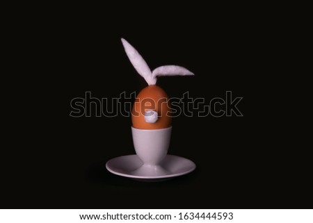 Easter bunny egg with cotton tail and ears on dark background with copyspace. Moody minimalistic decoration concept. Stock photo.