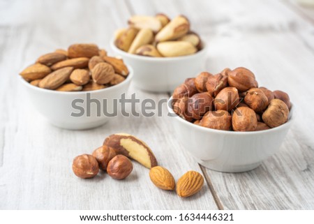 Different nuts in the white bowl on lignt wood table with copy space. Almond seeds, hazlenuts and brazilian nuts. Stock photo