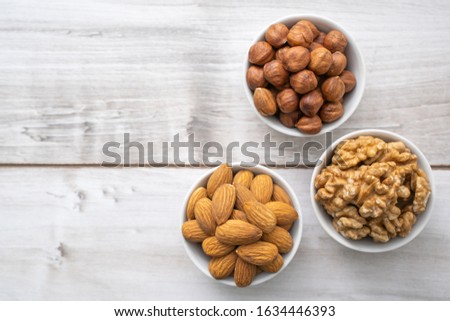Different nuts in the white bowl on lignt wood table with copy space, top view. Almond seeds, walnuts and hazlenuts. Stock photo, commercial banner template.