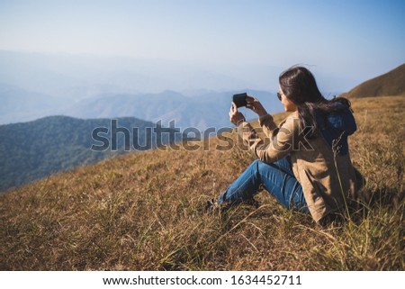 The back view of An asian woman traveler is sitting And take pictures of the mountains with a mobile phone

