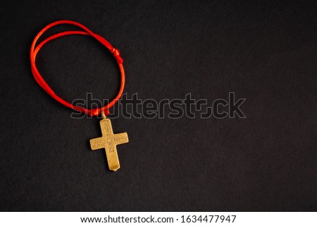 Christian cross on a red rope, on a black background with an empty place. Stock photo cross top.