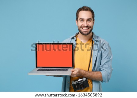 Smiling traveler tourist man in summer clothes with photo camera isolated on blue background. Passenger traveling abroad on weekends. Air flight journey. Holding laptop pc computer with empty screen