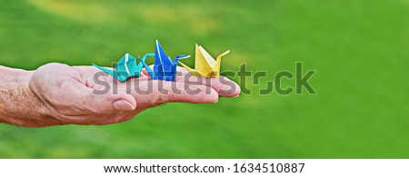 Traditional Japanese paper crane on male hand as symbol of peace and happiness on green background. Male palm with colorful handmade paper cranes orizuzu with copy space, banner