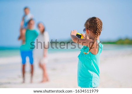 Little girl taking photo on phone of her family at the beach