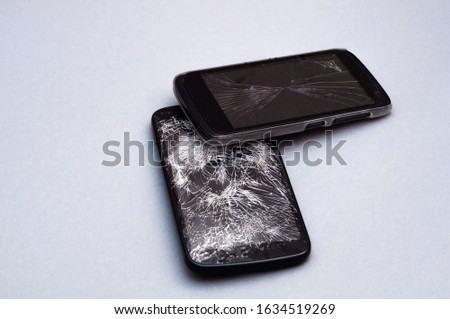 Two smartphone with broken screen on gray background.