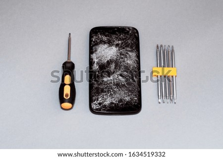 view from above on smartphone with broken screen and tools on gray background.