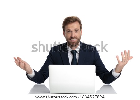 happy young businessman in navy blue suit smiling and sitting isolated on white background, full body