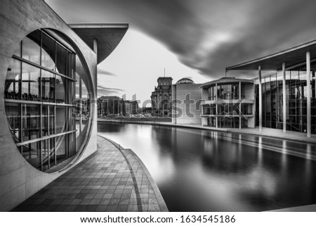 A grayscale shot of a lake in the middle of city buildings under a cloudy sky