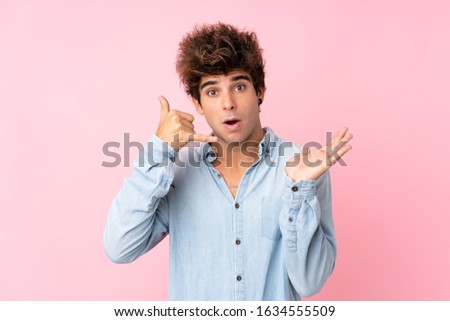 Young caucasian man with jean shirt over isolated pink background making phone gesture and doubting