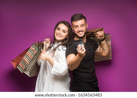 Shopping and leisure concept. Guy with beard and girl with smiling faces do shopping. Couple in love holds shopping bags on pink background. Man with beard holds credit card.