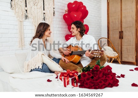 attractive woman listening boyfriend playing gutar while sitting on the bed, celebration st valetines day together Royalty-Free Stock Photo #1634569267