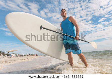 Paddle board fun SUP watersport fitness man carrying paddleboard after water surf session in Sanibel Island, Florida. USA summer travel fit active lifestyle.