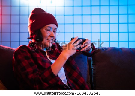 Teen girl exciting playing smart phone in a room lit with neon color at home.