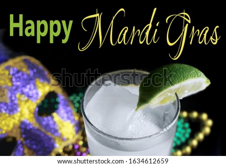 Alcoholic beverage and purple, green and gold Mardi Gras beads with mask on a black background for a festive February holiday image. The drink is a Gin Fizz garnished with a lime. Greeting added.