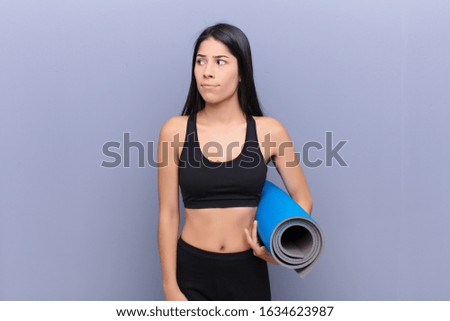 young pretty lating woman with a yoga mat against cement wall