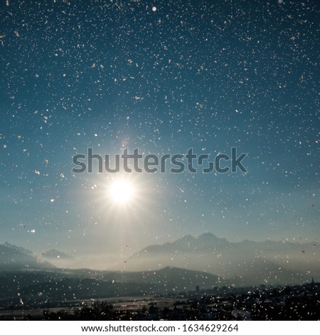 A picture of snowflakes with the sun and rocky mountains on the blurry background