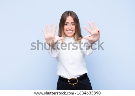 young pretty hispanic woman smiling and looking friendly, showing number nine or ninth with hand forward, counting down against blue wall