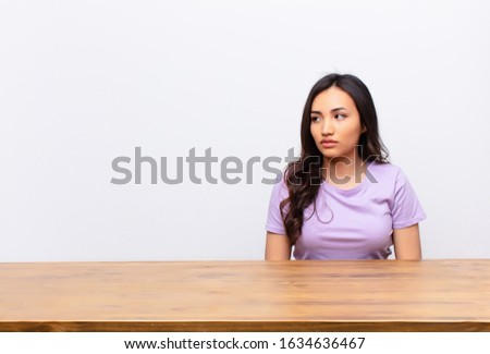 young latin pretty woman feeling sad, upset or angry and looking to the side with a negative attitude, frowning in disagreement against flat wall