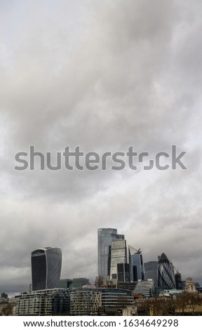 City of London in the UK. Portrait view over the River Thames to the city of London with dramatic grey stormy clouds. Cityscape of the business district of London with skyscrapers in 2020.