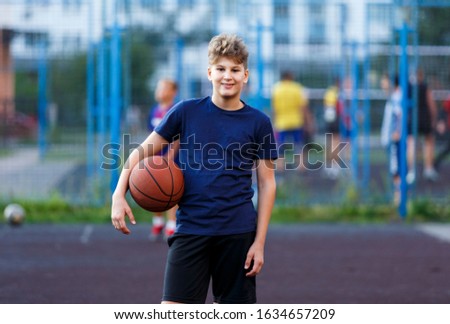 Cute smiling boy in blue t shirt plays basketball on city playground. Active teen enjoying outdoor game with orange ball. Hobby, active lifestyle, sport for kids.	