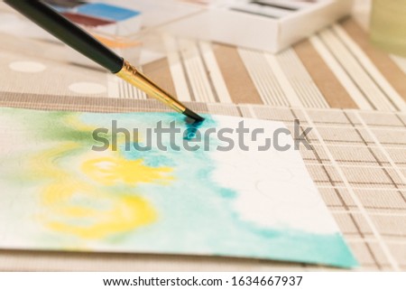 Blurred photo: hand draws with a brush a watercolor colored drawing, horizontal photo