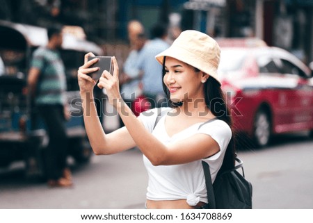 Young adult asian traveller happy woman in white shirt with backpack. Solo sightseeing with modern technology concept. She use smart phone. Beside landmark Khaosan Road. Bangkok City, Thailand