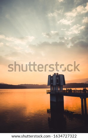 Vertical scenic landscape picture of the mesmerizing Tuyen Lam lake of Da Lat, Vietnam at sunset. The sun is setting behind the building, silhouettes of tourists standing on the bridge.