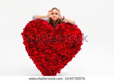 a girl with a huge red heart on a white background looks through fingers folded into a heart shape. Banner for the day of all lovers