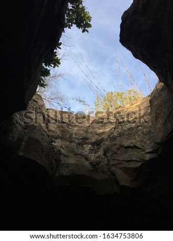 An opening from the dark depths of a cave exposing the brilliant outdoor illumination and blue sky.