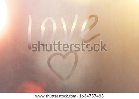 Inscription love and heart on the sweaty glass. love heart drawn on a misted glass window on the colorful background. symbol of love and happiness painted on the misted glass