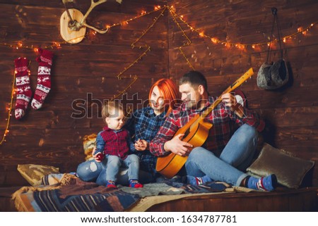 Family sitting at home. Father playing on a guitar.
