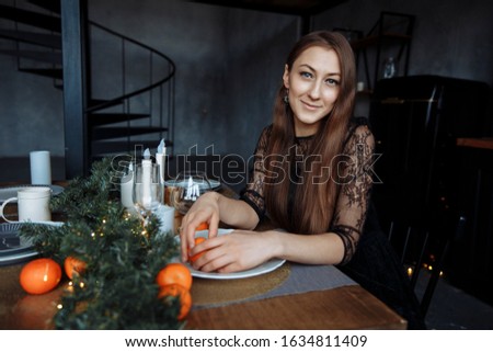 Brunette in a black dress cleans an orange in a beautiful New Year setting