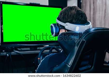 Young man play game with virtual reality glasses on simulator chair and steering wheel. Chroma key green screen