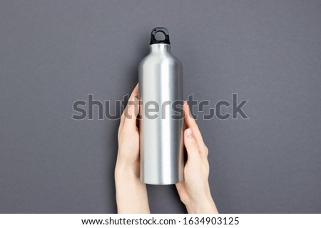 Female hands hold metal bottle and mug. Zero waste concept on dark gray background.