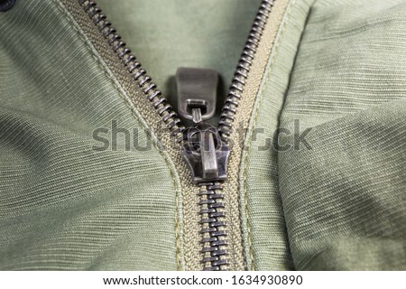 Fragment of partially fastened metal zipper fastener with metal puller on the outerwear olive color close-up at shallow depth of field
