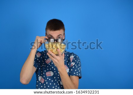 man in 3D glasses hid behind popcorn on a blue background