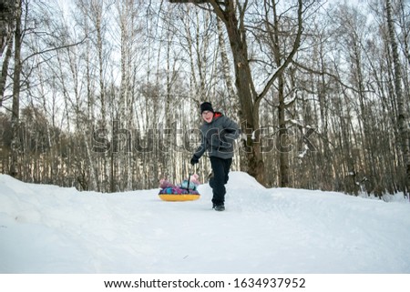 the boy runs in the snow and carries a little sister on a tubing. winter holiday concept