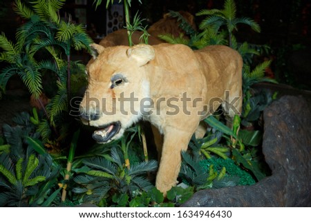 Brown Lion Animal Figure Statue . Statue lion . Life size replica model . The lion is in an artificial green forest at night.